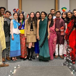 A group of happy international students posing together. In the background, you can see international flags decorating the room.